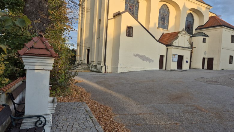 Trinkbrunnen, © Weinviertel Tourismus GmbH Kirche mit gelber Fassade und roten Dächern, umgeben von Herbstlaub und Bäumen.