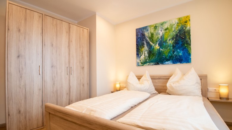 Rebenhof, Ferienwohnung, © Rebenhof Ein gemütliches Schlafzimmer mit einem Doppelbett, Holzmöbeln und einem bunten Gemälde an der Wand.
