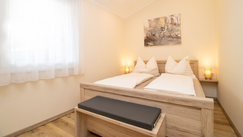 Rebenhof, Ferienwohnung, © Rebenhof Ein gemütliches Schlafzimmer mit einem Doppelbett aus Holz, zwei Nachttischlampen und einem Bild an der Wand.
