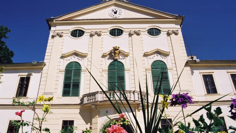 Kirchstetten, © Gemeinde Neudorf/ Staatz Historisches Gebäude mit grünen Fensterläden und Uhr auf der Fassade, umgeben von bunten Blumen.
