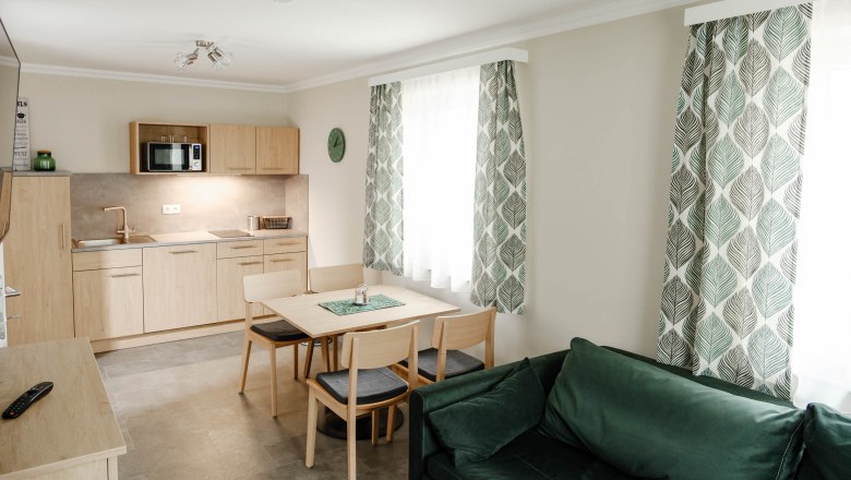 Küche Grüner Veltliner, © Michael Reidinger Moderne Küche mit Holzmöbeln, Esstisch, grünen Vorhängen und Sofa.