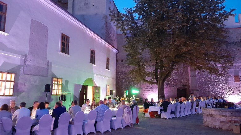 Tafeln im Weinviertel, © Weinviertel Tourismus GmbH Abendveranstaltung im Freien mit gedeckten Tischen und Gästen vor einer beleuchteten historischen Mauer.