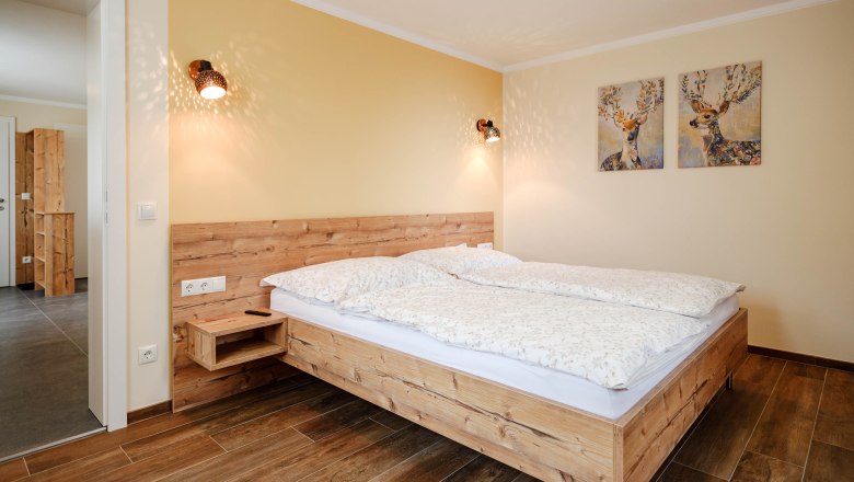 Schlafzimmer Gelber Muskateller, © Michael Reidinger Gemütliches Schlafzimmer mit Holzbett und Hirschbildern an der Wand.