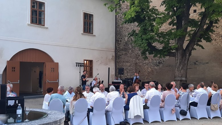 Tafeln im Weinviertel, © Weinviertel Tourismus GmbH Menschen sitzen an einem langen Tisch im Freien, umgeben von historischen Gebäuden und Bäumen.