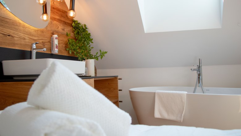 Freistehende Badewanne für gemütliche Stunden, © Hintersteiner Gerald Lifedesign Modernes Badezimmer mit Badewanne, Waschbecken, Pflanzen und Dachfenster.