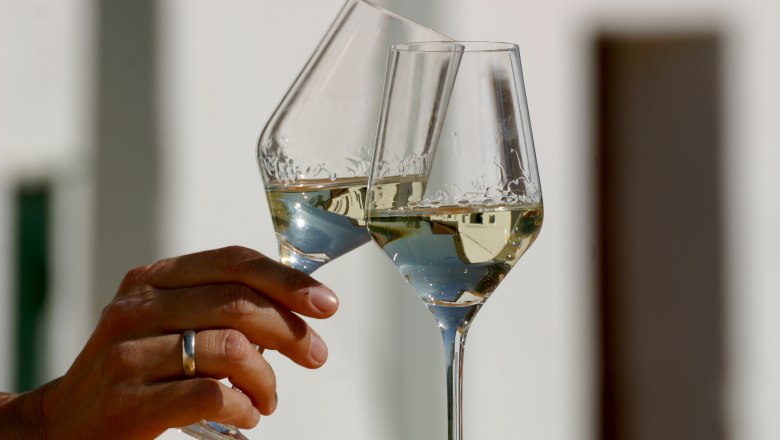 Zum Wohl!, © Rudi Weiss Zwei Weingläser stoßen an, gefüllt mit Weißwein.