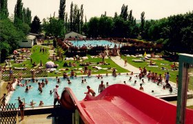 Freibad Neusiedl/Zaya, © Gemeinde Neusiedl/Zaya Ein Freibad mit mehreren Pools, einer roten Wasserrutsche und vielen Menschen, die im Wasser schwimmen oder auf der Wiese liegen.