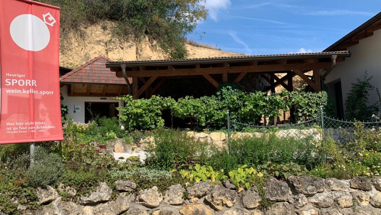 Wein.Keller.Sporr, © Familie Sporr Außenansicht eines Heurigen mit Garten und Werbeschild.