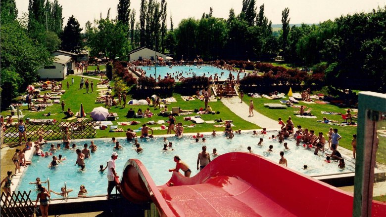 Freibad Neusiedl/Zaya, © Gemeinde Neusiedl/Zaya Ein Freibad mit mehreren Pools, einer roten Wasserrutsche und vielen Menschen, die im Wasser schwimmen oder auf der Wiese liegen.
