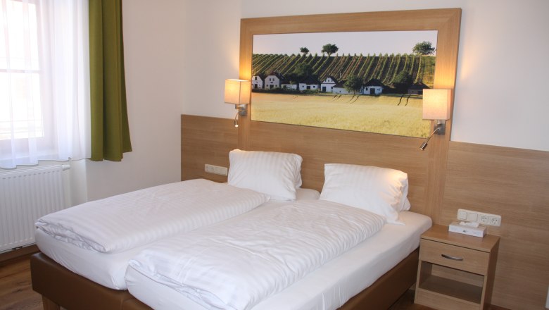 Gästezimmer, © Familie Rieder Ein Gästezimmer mit einem Doppelbett, Holzverkleidung, Nachttisch und einem Bild von Weinbergen an der Wand.