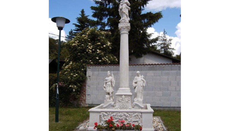 Mariensäule, © Gemeinde Hauskirchen Mariensäule mit Statuen und Blumen, umgeben von Bäumen und einer Mauer.