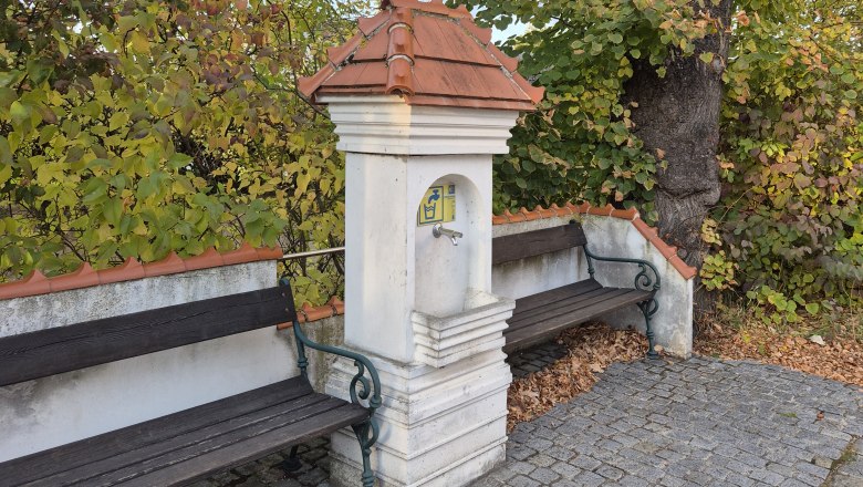 Trinkbrunnen in Drasenhofen, © Weinviertel Tourismus GmbH Zwei Bänke an einem kleinen Brunnen in einem herbstlichen Park.