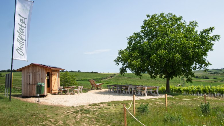 Rebenhof, Chillplatzl, © Rebenhof Ein Rastplatz mit Holzhütte, Tischen und Stühlen inmitten von Weinbergen unter einem Baum.
