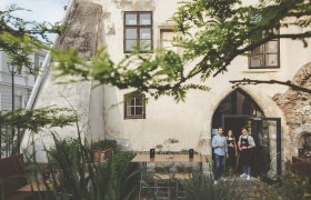 WeinStein Gastgarten, © Michael Reidinger Drei Personen stehen in einem historischen Innenhof vor einem Gebäude mit gotischem Bogenfenster.
