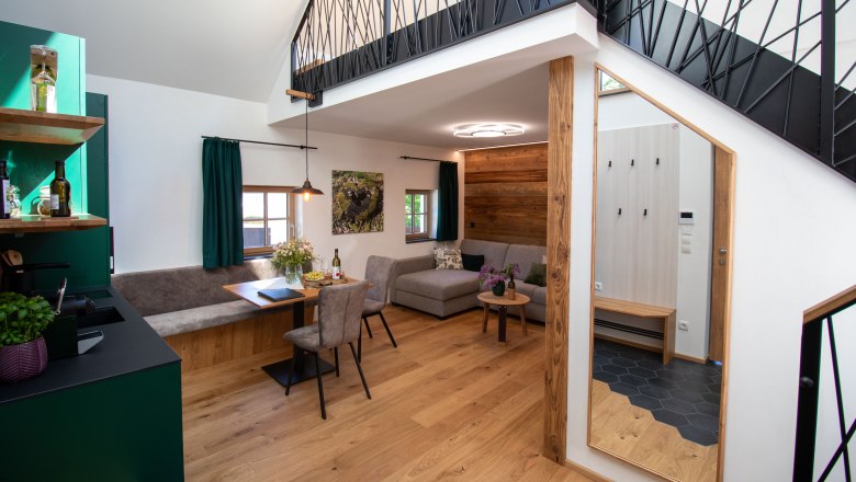 Modern eingerichtetes Kellerstöckl, © Hintersteiner Gerald Lifedesign Modernes Apartment mit Holzboden, grauem Sofa, Esstisch und offener Galerie.