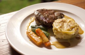 Ein Teller mit einem Stück Fleisch, Gemüse und einer Kartoffelbeilage.