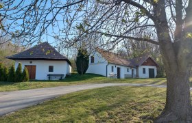 Weiße Gebäude mit roten Dächern in ländlicher Umgebung, Bäume im Vordergrund.