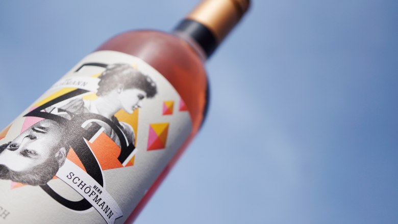 Nahaufnahme einer Weinflasche mit künstlerischem Etikett vor blauem Himmel.