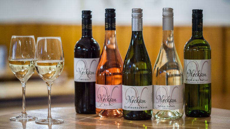 Fünf Weinflaschen und zwei gefüllte Weingläser auf einem Holztisch.