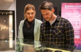 Zwei Personen betrachten Artefakte in einer Glasvitrine im Museum.
