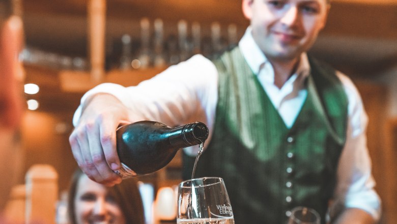 Ein Mann in traditioneller Kleidung schenkt Wein in ein Glas ein.