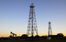 Zwei Bohrtürme und eine Ölpumpe bei Sonnenuntergang.