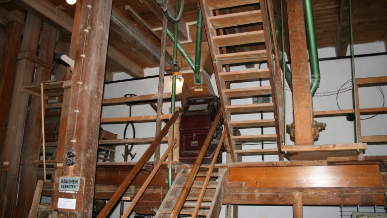 Innenansicht einer alten Mühle mit Holztreppen und Maschinen.