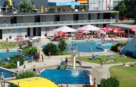 Außenbereich eines Schwimmbads mit mehreren Pools und Liegewiese.