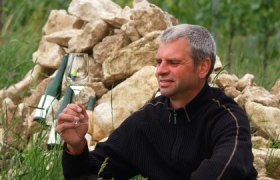 Mann hält Weinglas vor Steinhaufen im Freien.