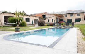 Ein moderner Hof mit einem gro&szlig;en Swimmingpool und Liegest&uuml;hlen im Vordergrund.