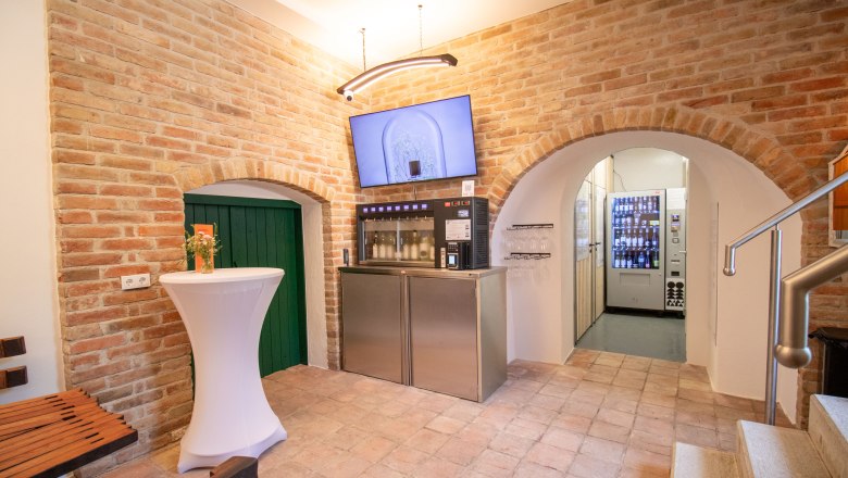 Innenansicht eines Verkostungsraums mit Ziegelw&auml;nden, einem Verkostungsautomaten und einem Stehtisch.