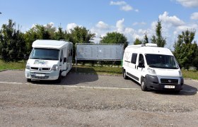 Zwei Wohnmobile auf einem Stellplatz mit Infotafel im Hintergrund.