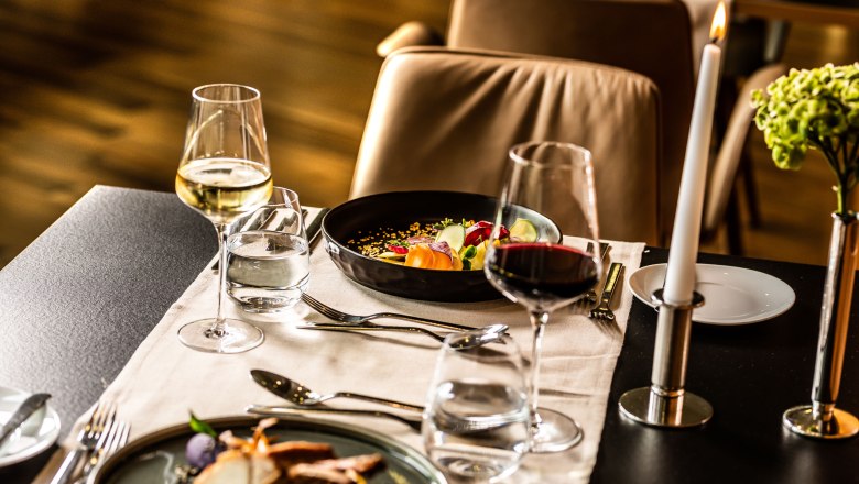 Eleganter Restauranttisch mit Weingläsern, Kerze und Gourmetgerichten.