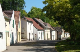 Reihe von Weinkellern in der Kellergasse Altlichtenwarth, umgeben von B&auml;umen.
