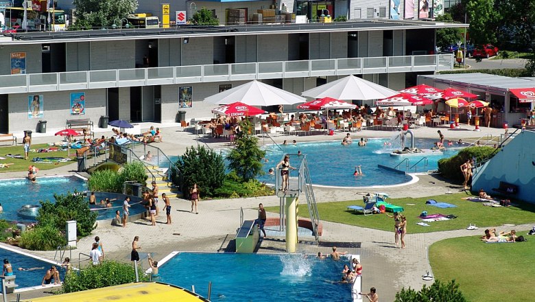 Außenbereich eines Schwimmbads mit mehreren Pools und Liegewiese.