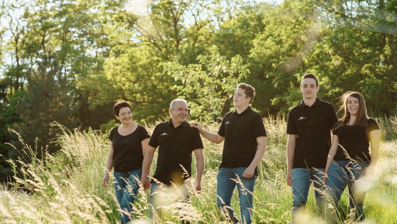Familie Sporr, © Michael Reidinger Eine Familie spaziert lächelnd durch eine grüne Wiese bei Sonnenschein.