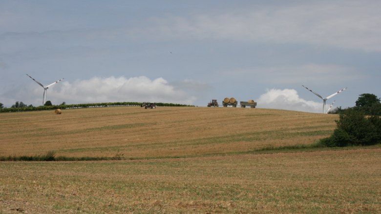 Landschaft mit Windrädern, Traktor und Heuballen auf einem Feld.