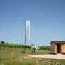 Ein kleiner Holzschuppen neben einem Weinberg mit einem Schild und einer Fahne mit der Aufschrift 'Chillplatz'.