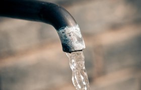 Nahaufnahme eines Wasserhahns mit flie&szlig;endem Wasser vor unscharfem Hintergrund.