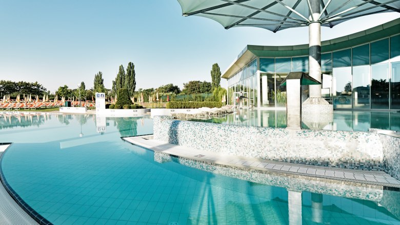 Außenbereich der Therme Laa mit Pool und Sonnenschirmen.
