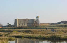 Ruine mit Turm und goldener Kugel in einer l&auml;ndlichen Landschaft mit Teich im Vordergrund.