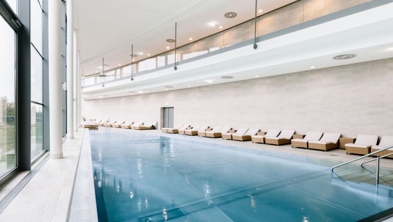 Innenansicht eines modernen Spa-Bereichs mit Pool und Liegestühlen.