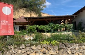 Außenansicht eines Heurigen mit Garten und Werbeschild.