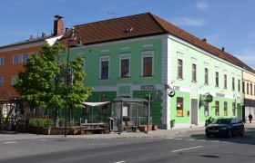 Grünes Gebäude mit Hotel- und Café-Schildern an einer Straßenecke.