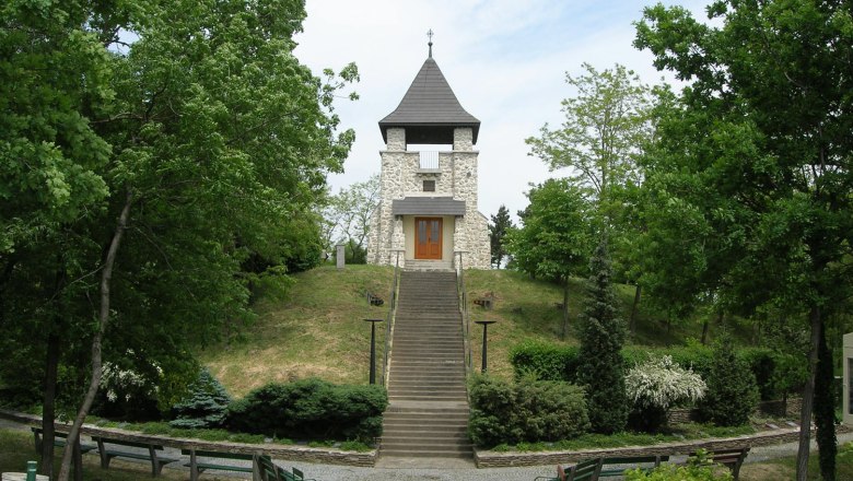 Ein steinernes Kriegerdenkmal mit Turm und Treppe, umgeben von Bäumen und Bänken.