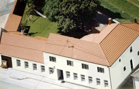 Luftaufnahme eines Gebäudekomplexes mit rotem Dach und Innenhof mit Bäumen und Spielplatz.