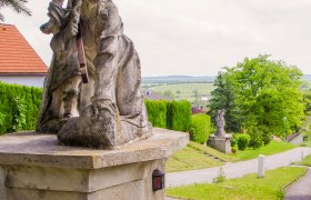 Steinstatue auf einem Sockel mit gr&uuml;ner Landschaft im Hintergrund.