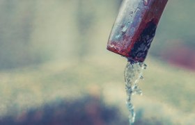 Nahaufnahme eines Trinkbrunnens mit fließendem Wasser aus einem Metallrohr.