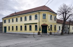 Gelbes zweist&ouml;ckiges Geb&auml;ude mit der Aufschrift 'Gasthaus M&uuml;ller'.
