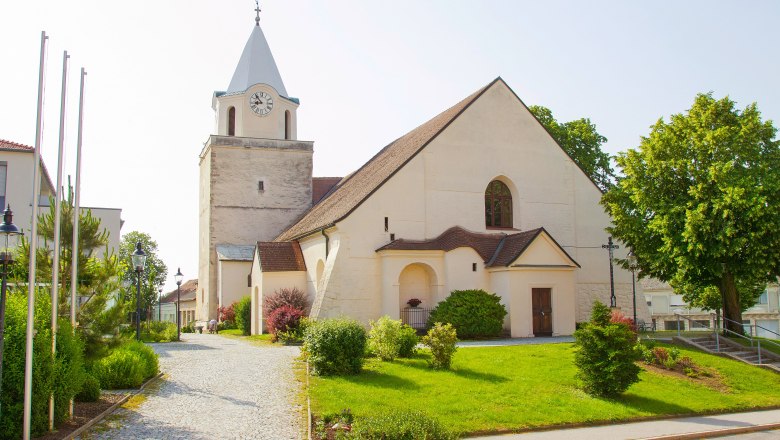 Eine Kirche mit einem Turm und Uhr, umgeben von einem gepflegten Garten und B&auml;umen.